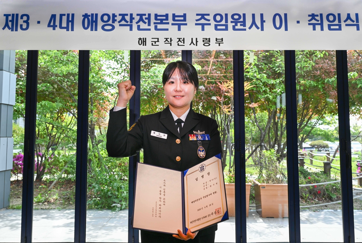 \"28日、釜山南区の海軍作戦司令部ネイビークラブで行われた海洋作戦本部主任元士の異動式で、ファン・ジヒョン元士（進）が任命証を手に記念撮影している。海軍提供\"