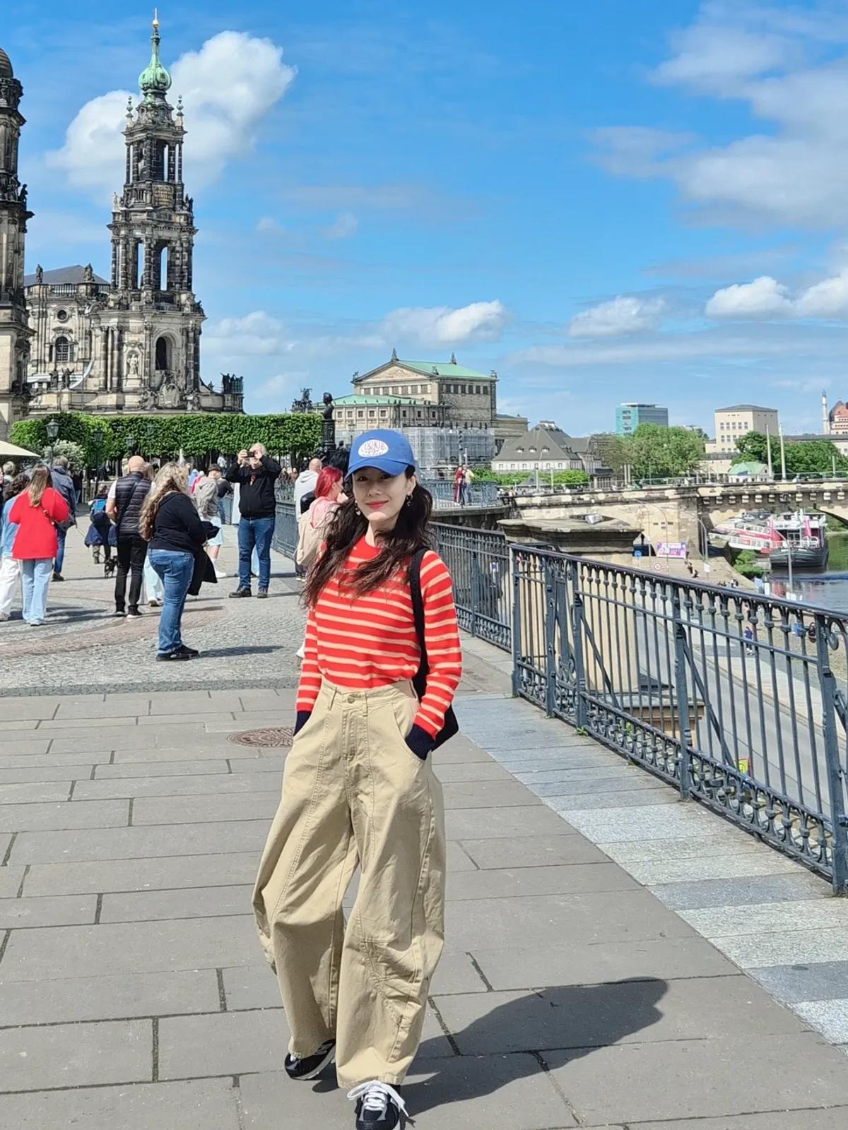 ドレスデンの川沿いで見かけたキム・ジス、ブラックのクロスボディバッグとスニーカーで仕上げた実用的な旅行スタイル