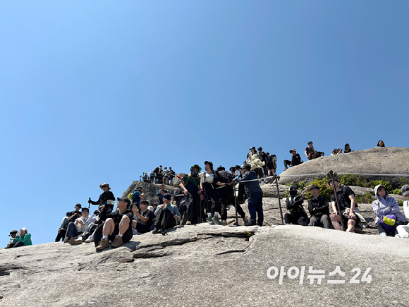 \"晴れ渡る春の日の9日、北漢山（북한산）白雲台（백운대）を訪れた登山客が記念撮影のために長い列を作っている\"