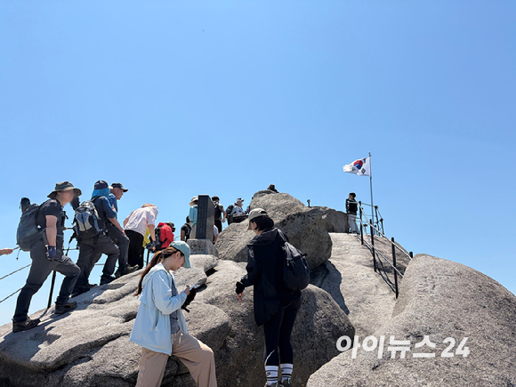 \"晴れ渡る春の日の9日、北漢山（북한산）白雲台（백운대）を訪れた登山客が記念撮影のために長い列を作っている\"