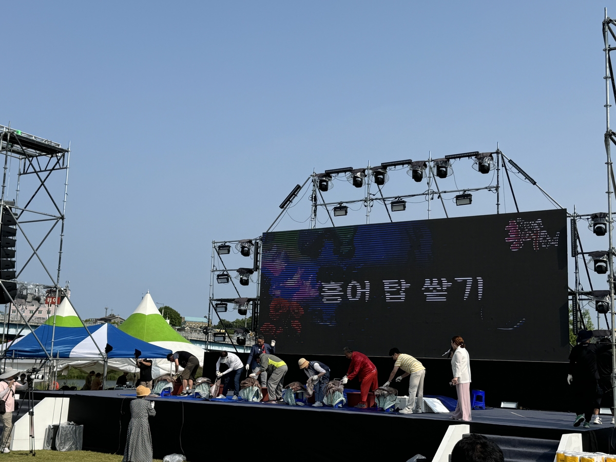 \"ヨンサンポのホンオ祭りの珍しい見どころ『ホンオの塔積み』に挑戦した参加者たちが、舞台の上でぬめるホンオを一尾ずつ慎重に積み上げている。　ナジュ市庁提供\"