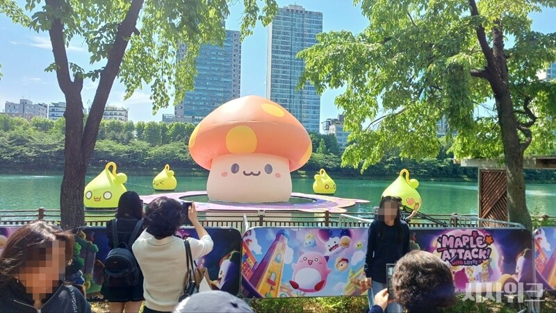 \"22日、ネクソンはソウル・松坡区の石村湖周辺を『メイプルストーリー』のIPキャラクターで彩り、『メイプルアタック！ウィズ・ロッテ』イベントを開始した。写真は石村湖の散策路で行き交う人々が写真を撮る様子。
